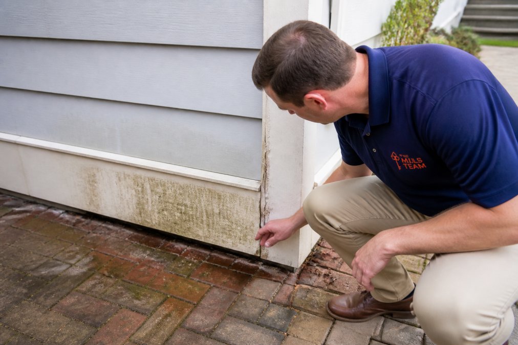 A homeowner inspecting the base of an exterior wall for water stains and caulking gaps on a coastal South Carolina home